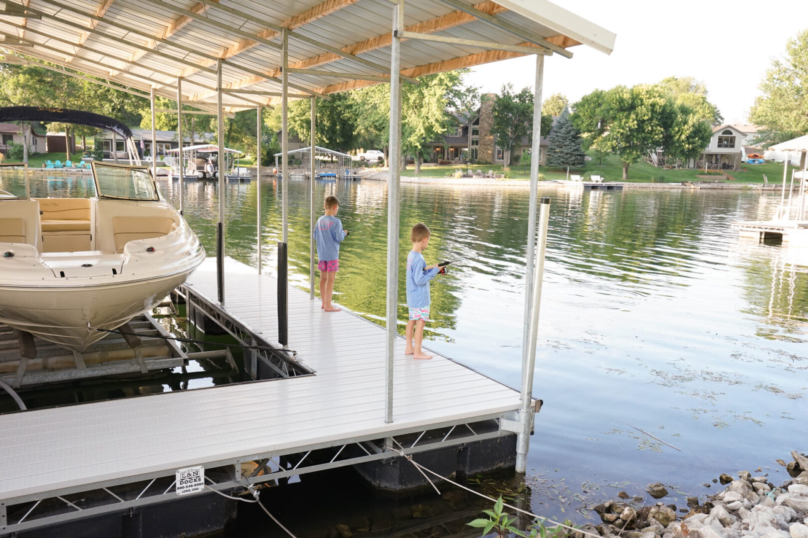 Two kids standing on a dock near the water.